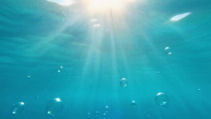 Underwater sunbeams filter through clear turquoise water, illuminating rising air bubbles, a serene natural phenomenon