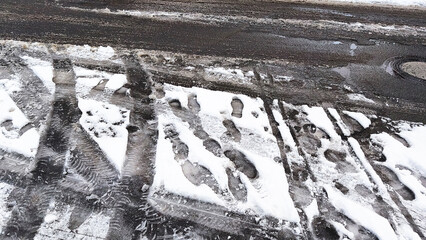 Footprints and tire tracks in melting snow on a wet urban street during winter