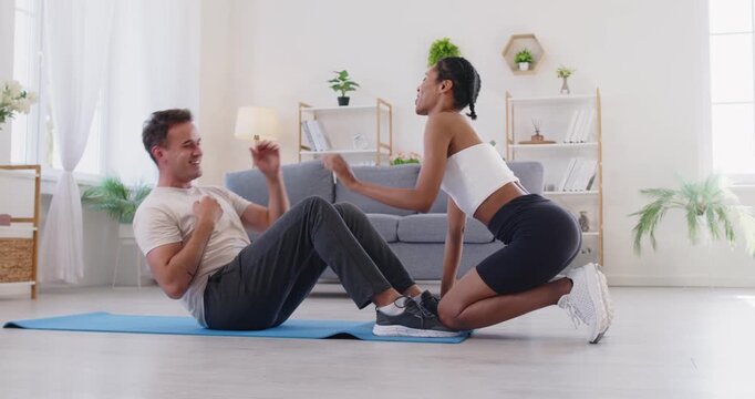 Couple fitness workout at home doing shaking press exercise. Man does crunches as his partner holds his feet, offering guidance and motivation to improve form. Sport, workout and healthy lifestyle