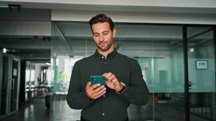 Young European business man manager ceo in green shirt using cell phone mobile app. Smiling Latin Hispanic male businessman holding smartphone in office workplace for trading, reading, working online - Powered by Adobe