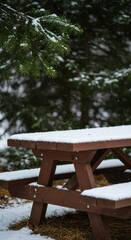 A rustic brown wooden picnic table stands outdoors, dusted heavily with fresh white snow, surrounded by lush green pine and fir branches ,evergreen ,outside ,forest