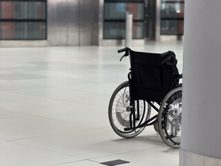 Close view of empty wheelchair positioned beside airport column copy space. Mobility assistance concept, accessibility services, inclusive travel environment, and support infrastructure in public