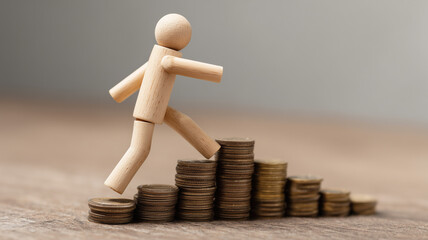 A wooden figure climbing stacks of coins, representing financial growth, career progress and personal economic advancement over time.
