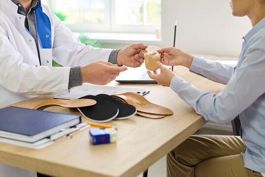 Prescription of custom insoles for flat feet correction and foot pain relief by male orthopedist at hospital consultation for woman. Doctor and patient holding insert to discuss fit, materials