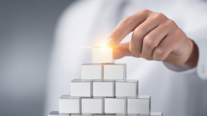 A hand stacking white blocks into a pyramid with a glowing top illustrating success building, hierarchy and structured growth concept.
