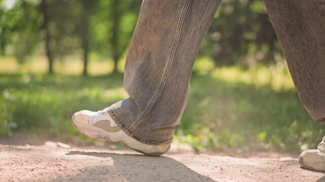 brisk park stride kicking up dust as scuffed sneakers push off from compacted dirt, loose denim sways, sunlit canopy and dappled shadow, frames show quickening pace with dynamic extension of leg,