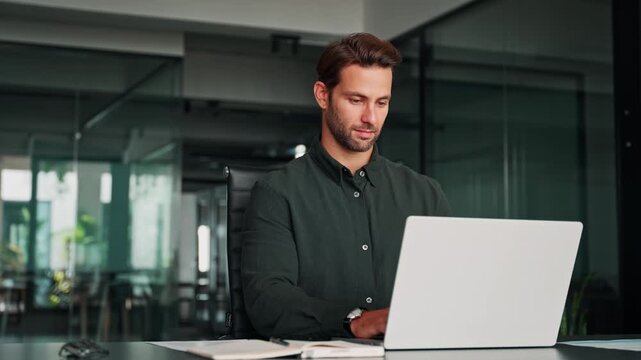 Focused business man salesman working on laptop computer reading financial contract document, writing notes in office. Young manager businessman specialist doing paperwork analysing on pc. Copy space
