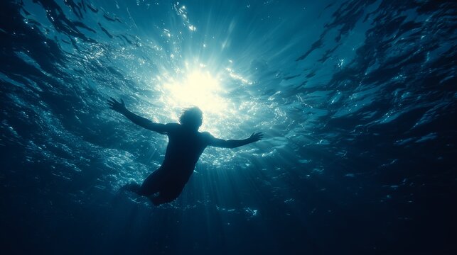 Silhouette of a swimmer emerging from deep blue ocean water with sunlight filtering through surface