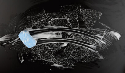 A bar of soap on a black surface with white foam, top view