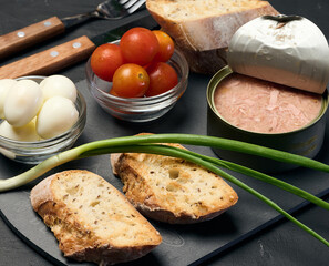 Can of tuna and fried baguette slices on black table, appetizer