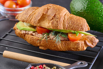 Crispy croissant filled with canned tuna, avocado wedges, boiled egg and cherry tomatoes, garnished...