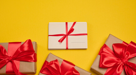 Gift boxes with red satin bow and stack of blank cards on yellow background