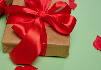 Gift boxes wrapped in craft paper and tied with a red satin bow on a green background.