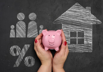 A woman's hands carefully hold a pink ceramic piggy bank against a black chalkboard