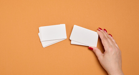 A woman's hand holds a stack of blank white business cards against a rich orange background.