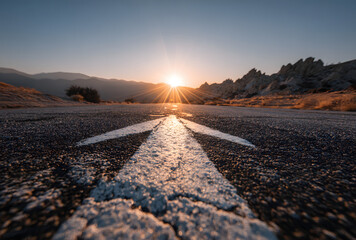 Asphalt road leads into the distance with a bright sunburst above, guiding the eye with a white arrow pointing upward and forward