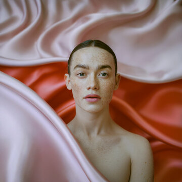 Retrato de belleza de mujer joven con pecas naturales envuelta en tela de seda rosa y roja