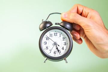 Alarm clock in hand on green background. Time management concept.