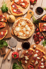 Pizzas with meat, mushrooms and pears on a round table with glasses of wine
