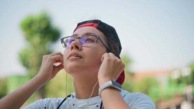closeup portrait adjusting earbuds in park, reflective profile with glasses and backward cap, meditator centering before run, student calibrating audio for podcast, listener enjoying ambient nature