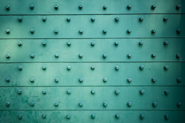 Weathered green metal door with horizontal panels and repeating hexagonal bolts creating a textured...
