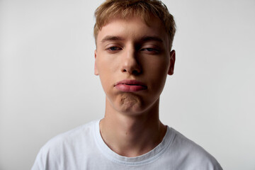 Fototapeta premium Pouty boy in white shirt makes a playful grimace, closeup shot highlighting facial expression, mood, studio lighting and a neutral, minimal background
