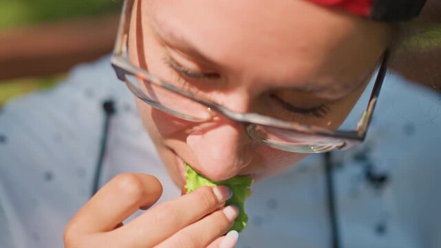 closeup woman tasting herb on bench home chef testing flavor, student sampling for study, mindful eater chewing slowly in sunlit park, glasses reflection, hoodie details, gentle chew, leaf texture