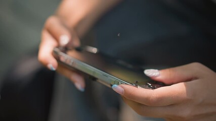closeup hands holding smartphone outdoors, manicured nails tapping touchscreen, stylish case reflecting sunlight, shallow depth of field, casual scrolling through apps, relaxed urban mood, influencer