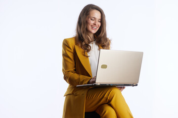 A businesswoman in a yellow suit laughs genuinely while interacting with her gold laptop, expressing happiness and satisfaction in her professional life.