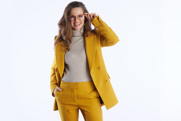 A professional woman in a stylish mustard yellow double-breasted suit smiles, confidently adjusting her glasses against a clean white background.