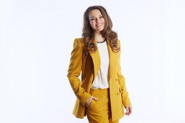 A confident professional woman in stylish mustard yellow pantsuit stands smiling against clean white background, exuding modern success and approachability. Her hand is casually tucked in pocket