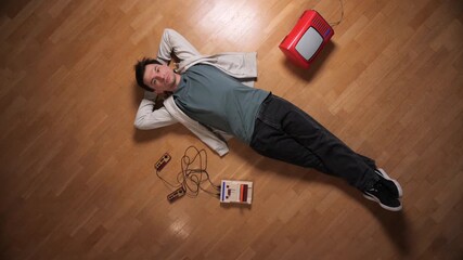 Man lying on a parquet floor with hands behind head, enjoying classic console video games on an old television, experiencing gaming nostalgia and relaxed leisure