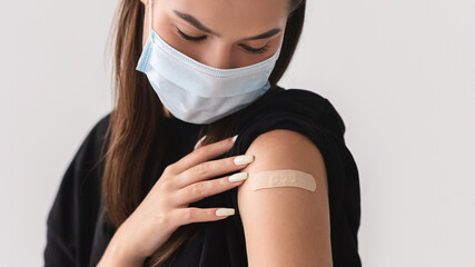Vaccination and healthcare during covid-19 epidemic. Young woman in face mask showing arm with band...