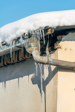 Frozen icicles forming on roof gutter, winter cold concept with ice details, rustic surface texture, and copy space.