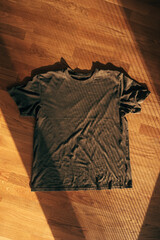 Casual T-shirt placed on hardwood flooring with soft directional light and visible texture, suitable as a clothing mockup or minimalist design background.