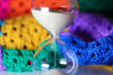 Hourglass sand glass as symbol of passing time and crocheted granny square blanket beautiful cozy handmade photo concept of time for relax hobby handiwork leisure autumn winter vibe  