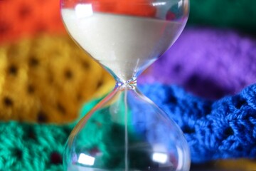 Hourglass sand glass as symbol of passing time and crocheted granny square blanket beautiful cozy handmade photo concept of time for relax hobby handiwork leisure autumn winter vibe  