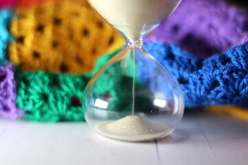 Hourglass sand glass as symbol of passing time and crocheted granny square blanket beautiful cozy handmade photo concept of time for relax hobby handiwork leisure autumn winter vibe  