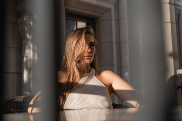 Woman, Sunlight, Window. Blonde woman sits at a table outdoors, bathed in warm sunlight streaming...