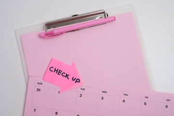 Medical check up reminder. Clipboard and pen on pink calendar background
