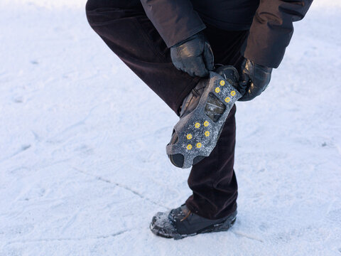 Man fastening winter traction cleats on boot while standing on icy surface.Concept of step-by-step product use, winter safety instruction, outdoor gear.