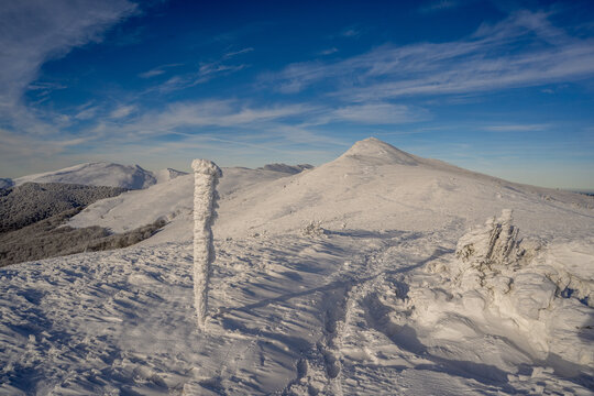 Frozen winter morning on Halicz peak in the Bieszczady Mountains. Snow-covered ridges, icy summit cross and clear sky along the popular Tarnica Halicz Rozsypaniec hiking loop.
