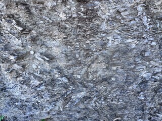 Natural rock surface with rough stone texture and layered mineral patterns. Gray rocky background formed by geological processes, ideal for abstract, nature, geology, construction or texture design.