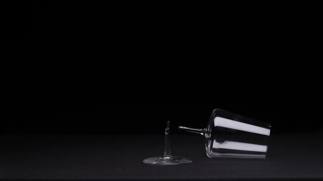 Broken wine glass with stem detached from bowl on dark surface, shards scattered to suggest fragility, accident, loss and irreparable damage in a studio setting