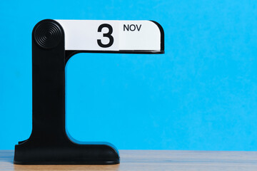 Modern flip calendar showing November 3 on wooden table with bright blue background.