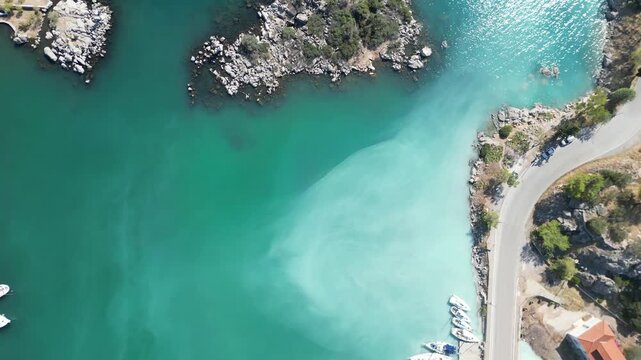 Cinematic top-down drone footage capturing the transition from a yacht marina with turquoise volcanic water to a small rocky island and the wild Mediterranean coastline