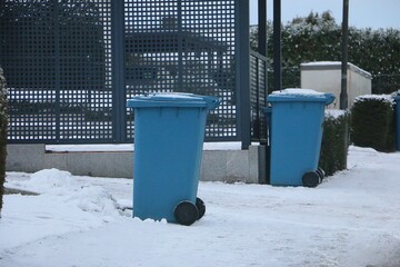 two blue plastic recycling bins for paper waste stands at the roadside, covered in snow, ready for collection