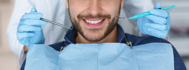 Cropped of smiling bearded man and dentist hands in blue robber gloves with dental tools, panorama. Unrecognizable male patient visiting dentistry, having regular checkup, closeup, web-banner