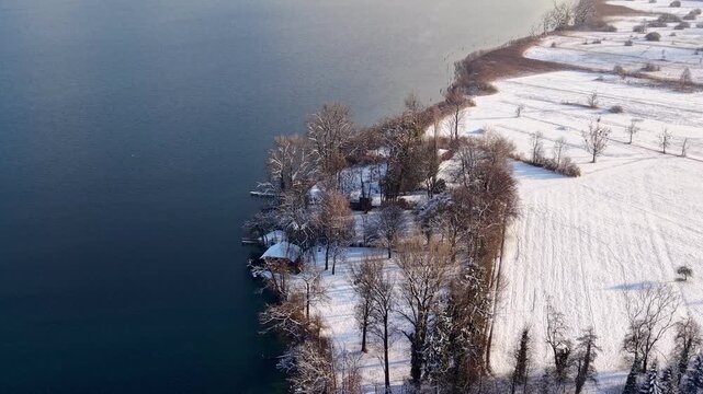 Aerial view of the snow-covered western shore of Lake Zug toward Risch, with Mount Rigi partly wrapped in clouds, creating a calm, atmospheric winter landscape.