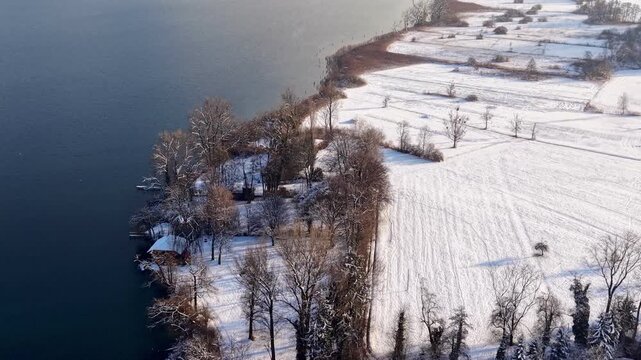 Aerial view of the snow-covered western shore of Lake Zug toward Risch, with Mount Rigi partly wrapped in clouds, creating a calm, atmospheric winter landscape.